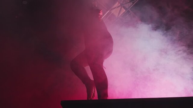 A striking silhouette of a dancer striking a dynamic pose in a room filled with dense pink and red fog. The conceptual lighting highlights the beauty of human movement and artistic expression.