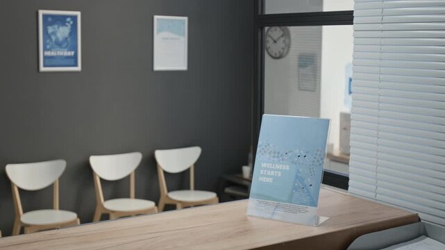 Acrylic stand with wellness flyer on wooden desk at reception area in modern hospital, chairs and posters on wall in background, copy space