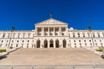 Obraz premium Front view of Sao Bento Palace, Portuguese Parliament building in Lisbon, Portugal, with grand staircase and neoclassical facade under clear blue sky. Travel and European government landmark concept.