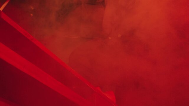 A dynamic low-angle shot of a woman headbanging and tossing her long hair wildly over a red ledge. Dense crimson fog and lighting create an aggressive, chaotic, underground rock concert vibe.