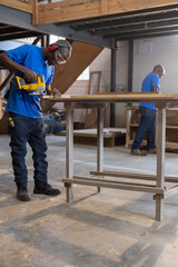Fototapeta premium African American male coworkers cutting wood with jigsaw and sorting lumber in workshop, copy space