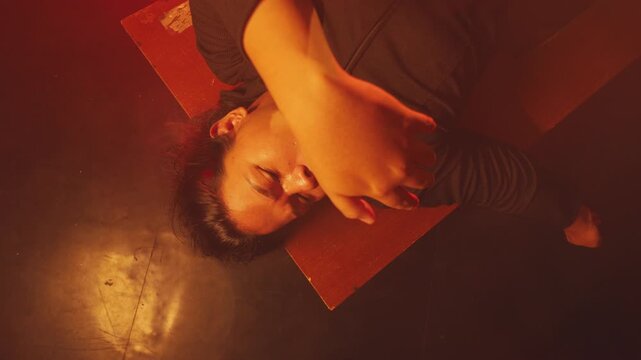 Top-down shot of a woman in a deep slumber as a blurry hand reaches toward her face. Set in a hazy, crimson-lit space, evoking themes of sleep paralysis, mysterious interventions, or haunting dreams.