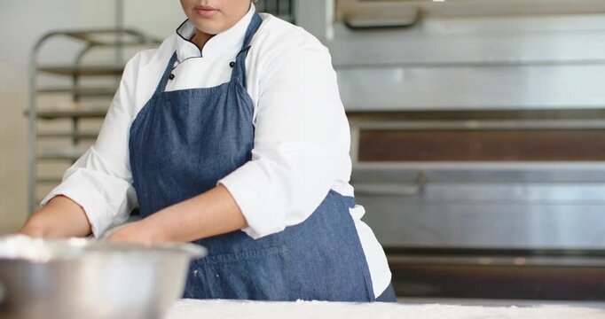 Vertical video: Dusting surface chef in coat denim apron stretching dough for baking at bakery