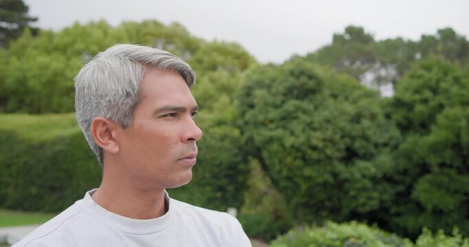 African American man turning toward camera, responding to reframing by pool hedge, wearing crewneck