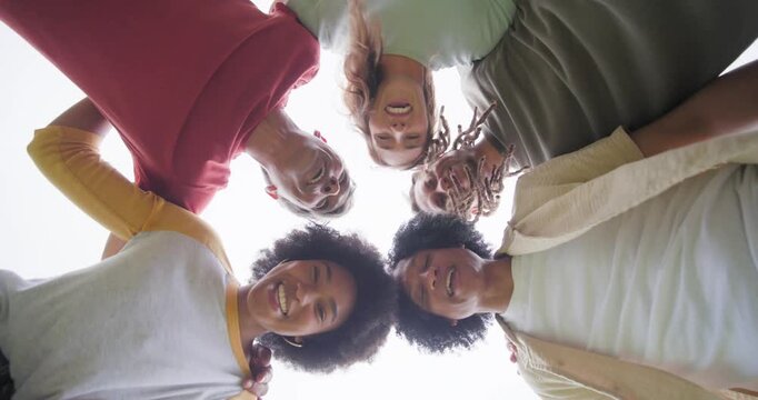 Diverse friends drawing to ground cam, leaning in while capturing low-angle shot, laughing outdoors