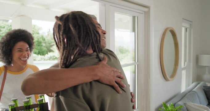 Diverse friends arriving at sliding door, man with dreads taking sixpack and carrying rose to visit