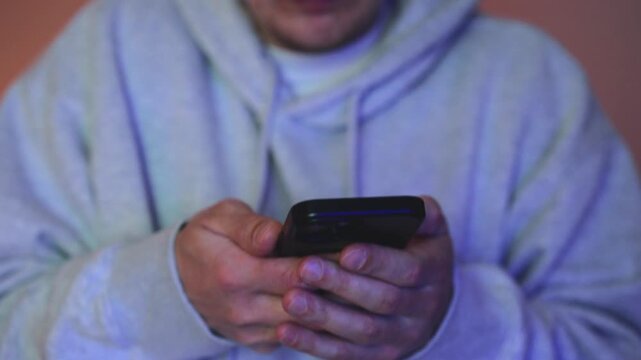 Close-up of trembling hands dialing emergency services on a smartphone. The person is visibly scared, fingers shaking while calling for help. Flashing police lights in the background