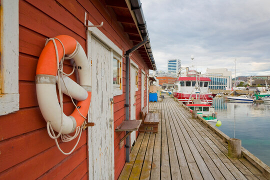 BOD&Oslash;, NORWAY - WOODEN PIER WITH TYPICAL RED PORT BUILDINGS - MARITIME SCENE WITH FISHING BOATS - NATURAL AFTERNOON LIGHT IN AUGUST - BRANDS AND TRADEMARKS REMOVED