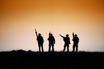 Obraz premium Silhouette of four soldiers with rifles standing on a hill at sunset