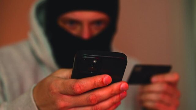 An anonymous criminal commits financial fraud, money transfer from a bank card and police lights flashing in the background