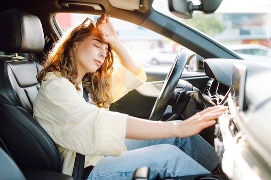 Woman sits behind wheel of car, placing hand on forehead, checking airflow. Beautiful female driver is tired and frustrated by heat on sunny summer day. Concepts: driver, heat, transportation.