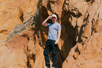 Young man stands on rocky cliffside, shielding eyes from sun © Reuben