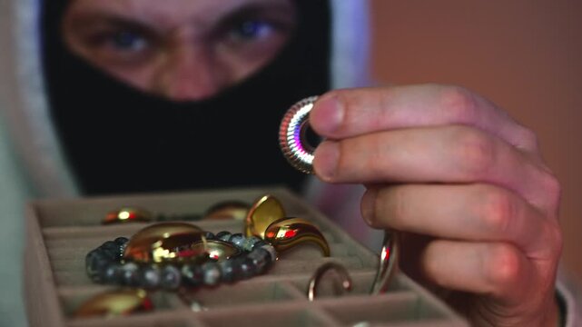 Robber with gold and jewelry in hand, police lights in the background.
An anonymous masked man commits a theft.