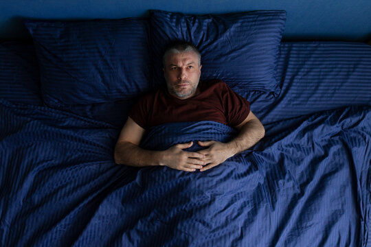 Insomnia. Middle aged man lying awake in bed at night staring upward