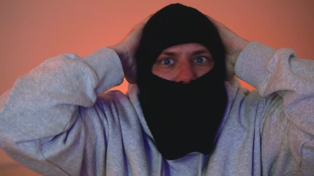 Arrest of masked criminal raising his hands with police lights in the background.
A dangerous criminal raises his hands and surrenders to the police.