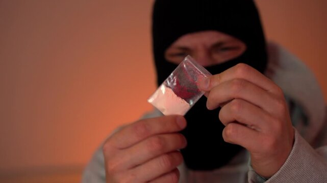 A man in a black balaclava holds a bag of narcotics.
Police lights are visible in the background, revealing a crime scene and drug trafficking.
A masked criminal is apprehended.