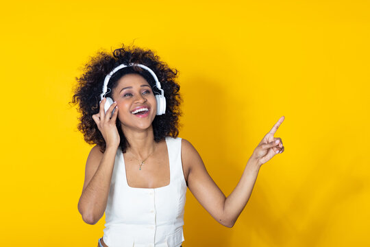 smiling young woman isolated on background with headphones pointing