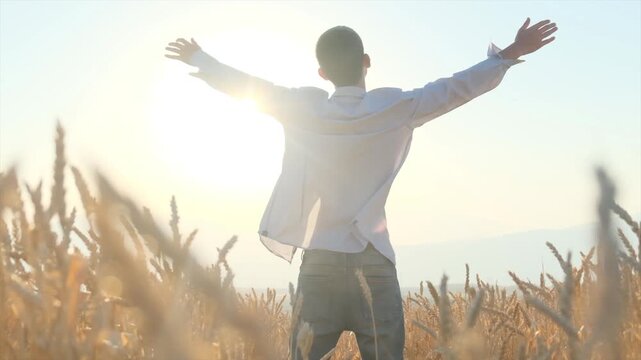Lonely tall slim young boy raises both hands to sun enjoying moment and thanking God. Guy in unbuttoned shirt among wheat field. Person happy to live.