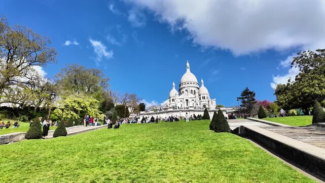 Low angle static shot of white clouds moving across a vibrant blue sky over the domes of the Sacr&eacute;-C&oelig;ur Basilica.