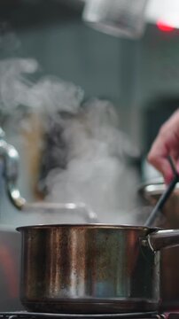 Chef stirring a boiling pot of soup with steam rising in a restaurant kitchen