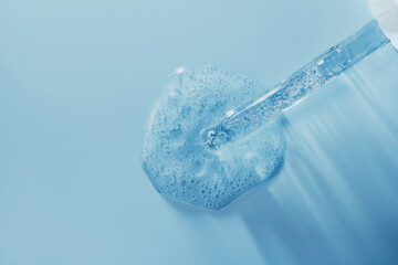 Pipette dripping transparent blue gel serum on blue background, perfect for skincare and cosmetic...
