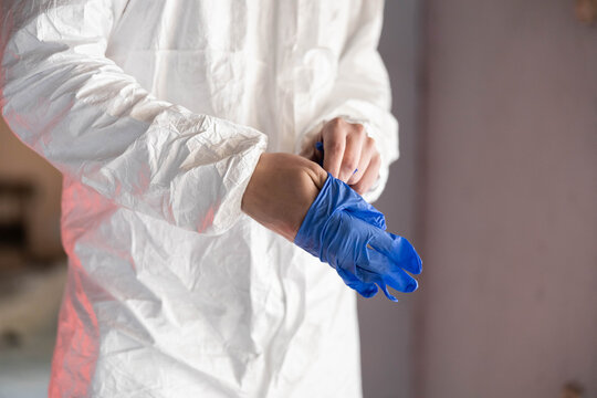 Professional preparing for work, wearing protective hazmat suit and blue medical gloves for safety against virus and disease