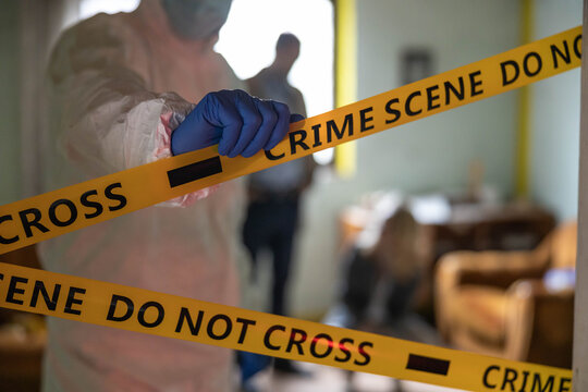 Forensic investigator placing yellow crime scene do not cross tape at a location, indicating a restricted area for investigation