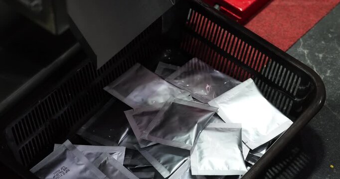 Sealed foil sachets gathered in plastic container after packaging line process. Industrial food or product packaging stage with modern automated equipment in factory.