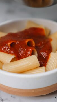 Chef adding fresh basil garnish to a traditional rigatoni pasta with tomato sauce