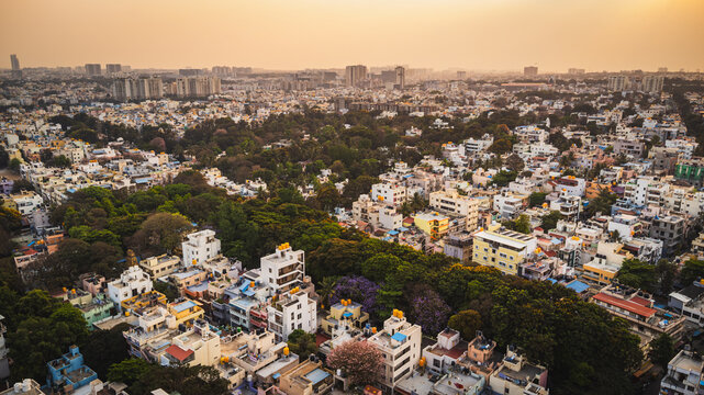 Aerial view of Bangalore city, Karnataka, India, showing a vast urban landscape with dense residential neighborhoods, modern development, and a lake surrounded by the expanding metropolis.