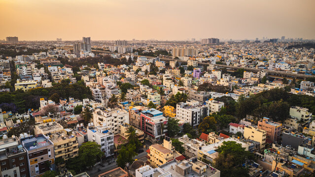 Aerial view of Bangalore city, Karnataka, India, showing a vast urban landscape with dense residential neighborhoods, modern development, and a lake surrounded by the expanding metropolis.