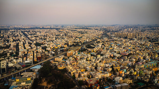Aerial view of Bangalore city, Karnataka, India, showing a vast urban landscape with dense residential neighborhoods, modern development, and a lake surrounded by the expanding metropolis.