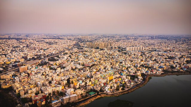 Aerial view of Bangalore city, Karnataka, India, showing a vast urban landscape with dense residential neighborhoods, modern development, and a lake surrounded by the expanding metropolis.