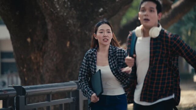 Two young scared asian students looking at something shocking. The man is pointing at something, then they start running away in fear and horror