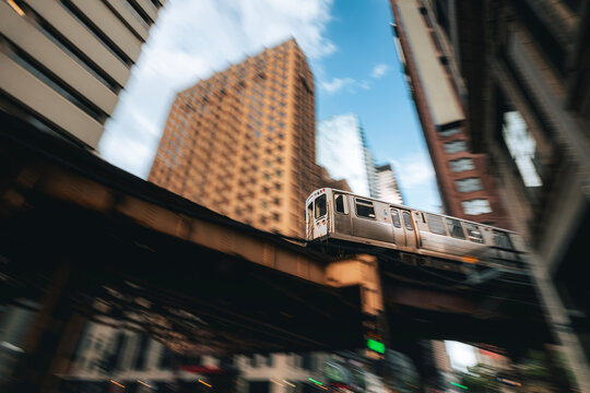 Train of public transportation on the move on elevated railway above street in downtown Chicago. Urban transport, city life, infrastructure, and daily commute concept.