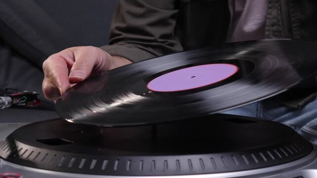 Hand carefully placing a black vinyl record with a purple label onto a modern dj turntable, highlighting analog music experience and retro sound culture
