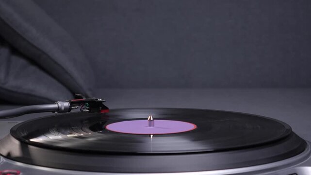 Turntable system playing a black vinyl record with a purple label and tonearm stylus making contact, generating sound for a retro music listening experience