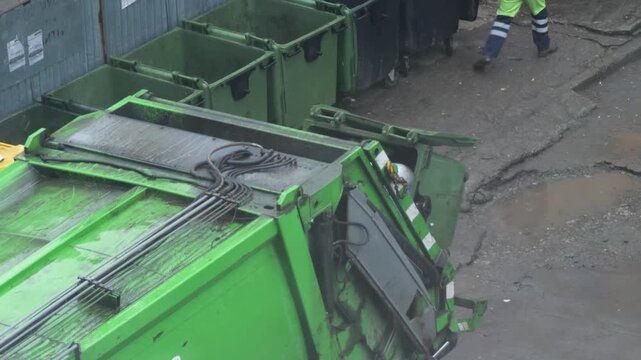 Hydraulic lift mechanism of a garbage truck emptying a trash container in the city. Professional municipal worker managing the waste collection process in a residential neighborhood.
