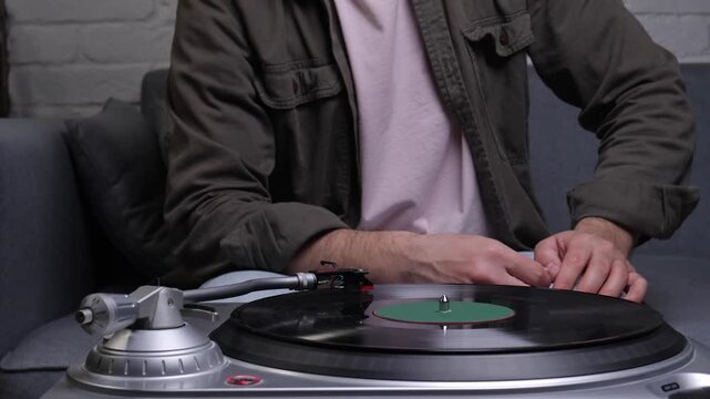 Man adjusting tonearm on a silver turntable as a black vinyl record spins, enjoying nostalgic analog sound at home close up of hands, hobby, relaxation and music passion