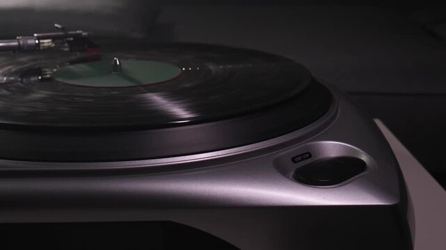 Hand pressing illuminated start stop button on silver turntable as dusty vinyl record is cued to spin, beginning vintage analog music playback for listening or dj use