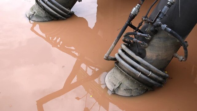 industrial suction pipes with hydraulic systems submerged in calm muddy water