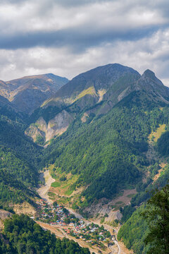Beautiful mountain landscape of Gabala, Azerbaijan. Deep green forests of the Caucasus under a cloudy sky, with a small village below.