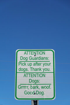 Rectangular sign with green text on a white background. It says, "ATTENTION Dog Guardians: Pick up after your dogs. Thank you. ATTENTION Dogs: Grrrrr, bark, woof. Good Dog." 