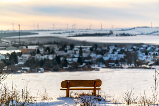 Holzbank an einem Aussichtspunkt mit Blick auf ein kleines Dorf im Winter