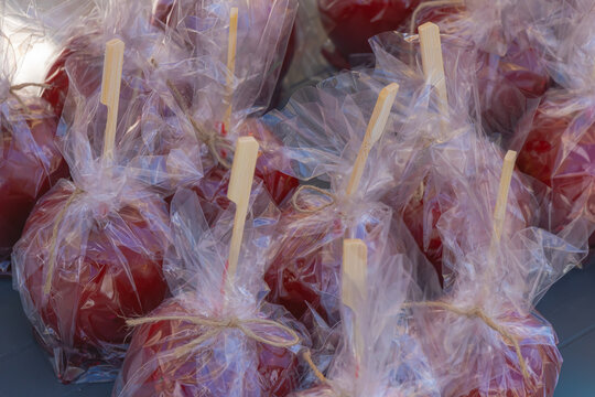 Candied apples wrapped in clear plastic with wooden sticks at market stall festive sweet treats close up