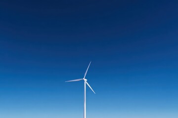 Fototapeta premium Wind turbine generating clean renewable energy against blue sky