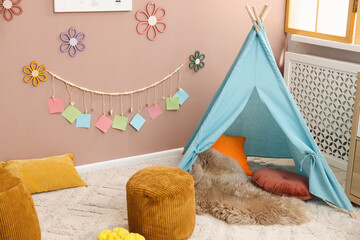 Colorful paper notes and beautiful decor hanging on beige wall near toy wigwam in stylish children's room. Interior design © New Africa