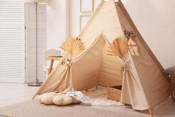 Stylish wigwam with dry leaves in child's room. Space for text © New Africa