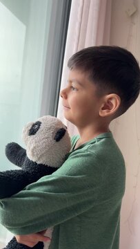 Thoughtful smling child looking through window holding toy