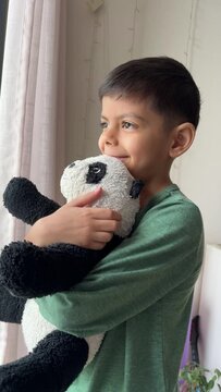 Thoughtful smling child looking through window holding toy
